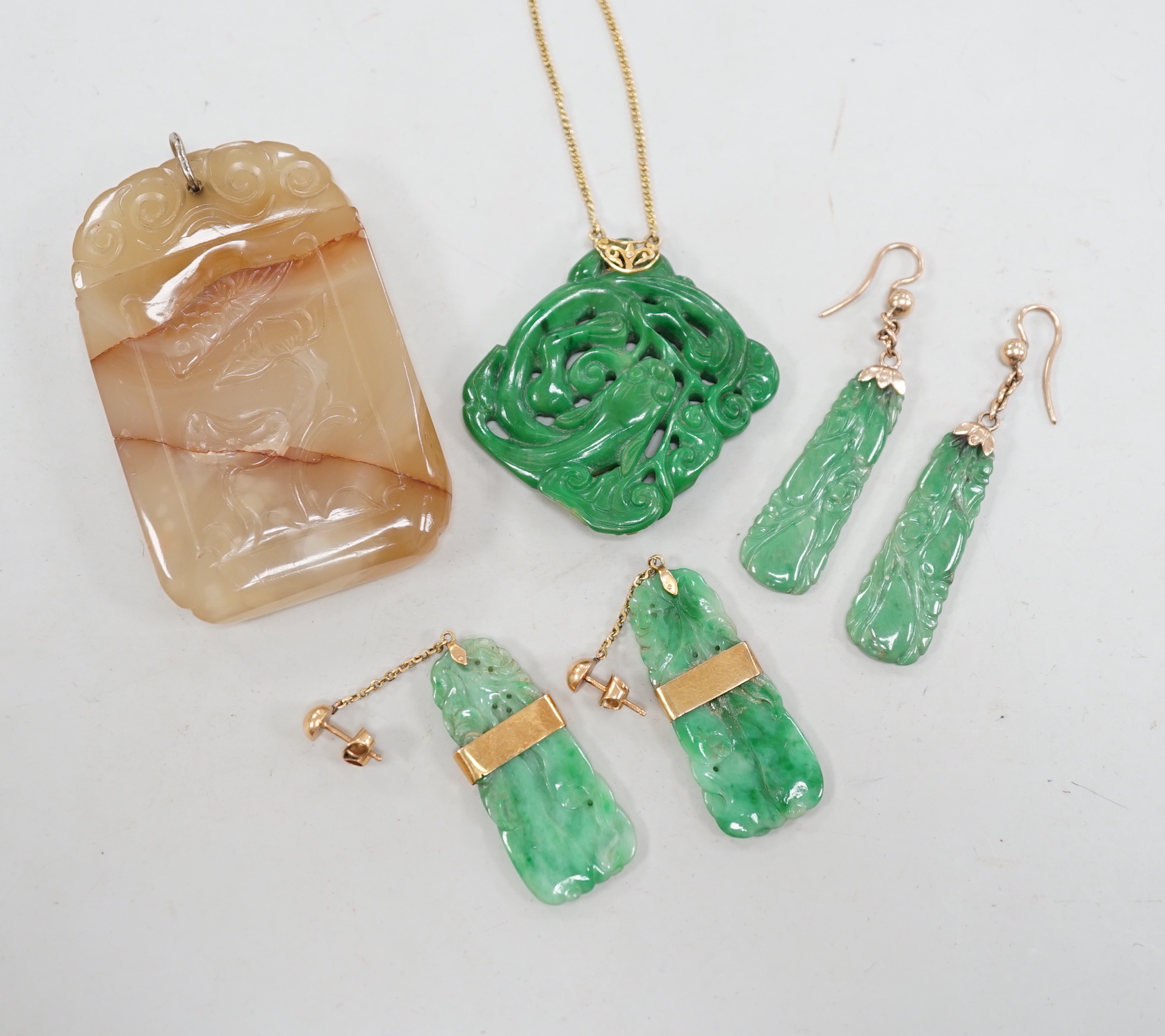 A Chinese carved hardstone pendant, 64mm, a pierced green hardstone pendant on chain and two pairs of yellow metal mounted carved jade earrings.